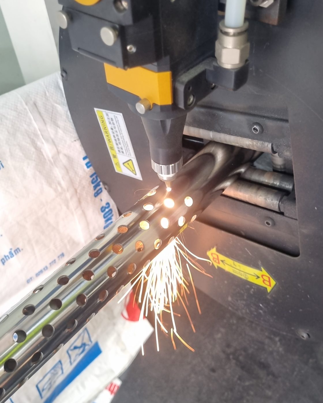 Đầu laser đang đục dãy lỗ tròn trên ống inox, tia lửa bắn ra